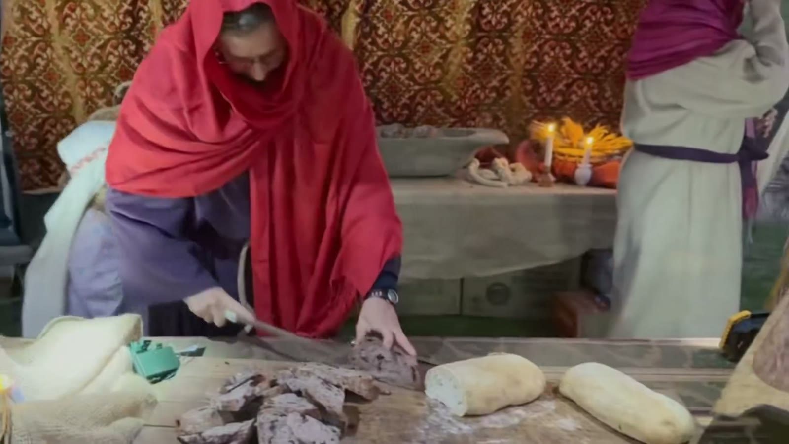 A baker in a red head scarf shapes loaves on a board