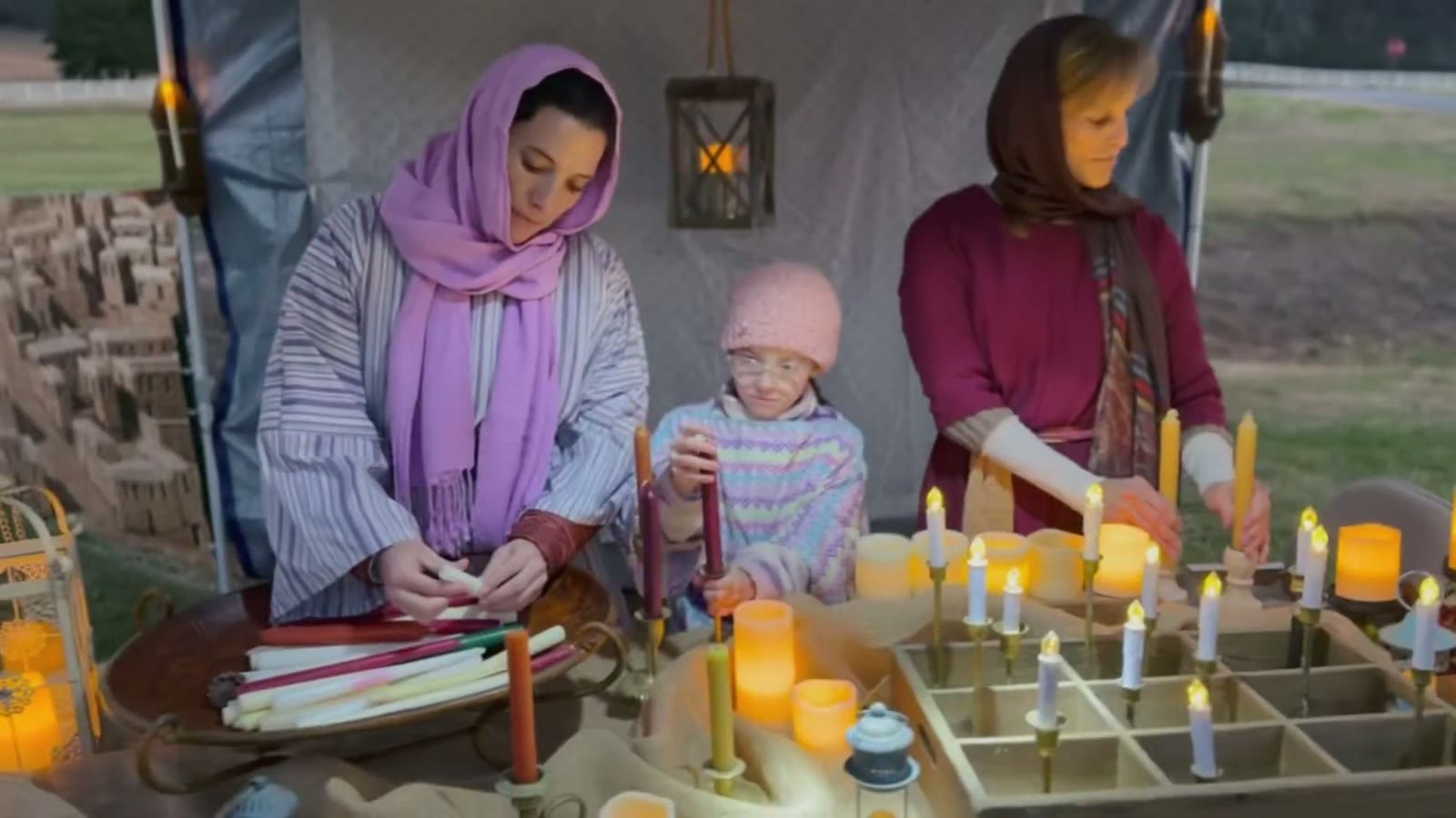 Women and a child dip candles at a table full of lit tapers