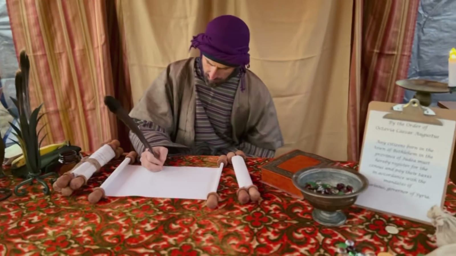 A tax collector in a purple turban writes names on a scroll
